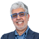 Smiling older man with gray hair, blue glasses, and a blue blazer over a button-up shirt, facing the camera against a white background—ready to represent Cybericon2024.