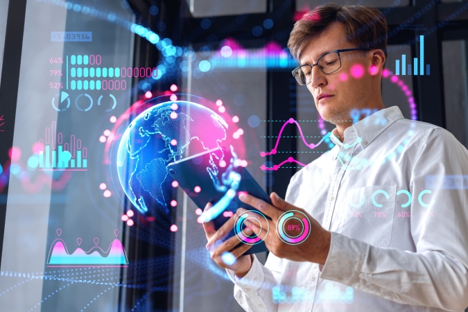 A man in glasses uses a tablet with various digital graphs, new data charts, and a holographic globe superimposed in front of him, suggesting data analysis or futuristic technology.